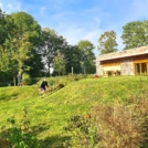 Afbeelding van een groene heuvel met rechtsachter een gebouw en linksachter bomen. In het midden twee rennende kinderen